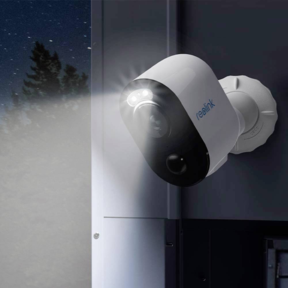 Security camera mounted on an exterior wall, showing a blue night sky. It is illuminated and monitoring the area with infrared light.