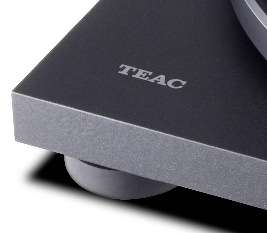 Corner of a TEAC turntable on a black background, focus on surface texture and brand logo.