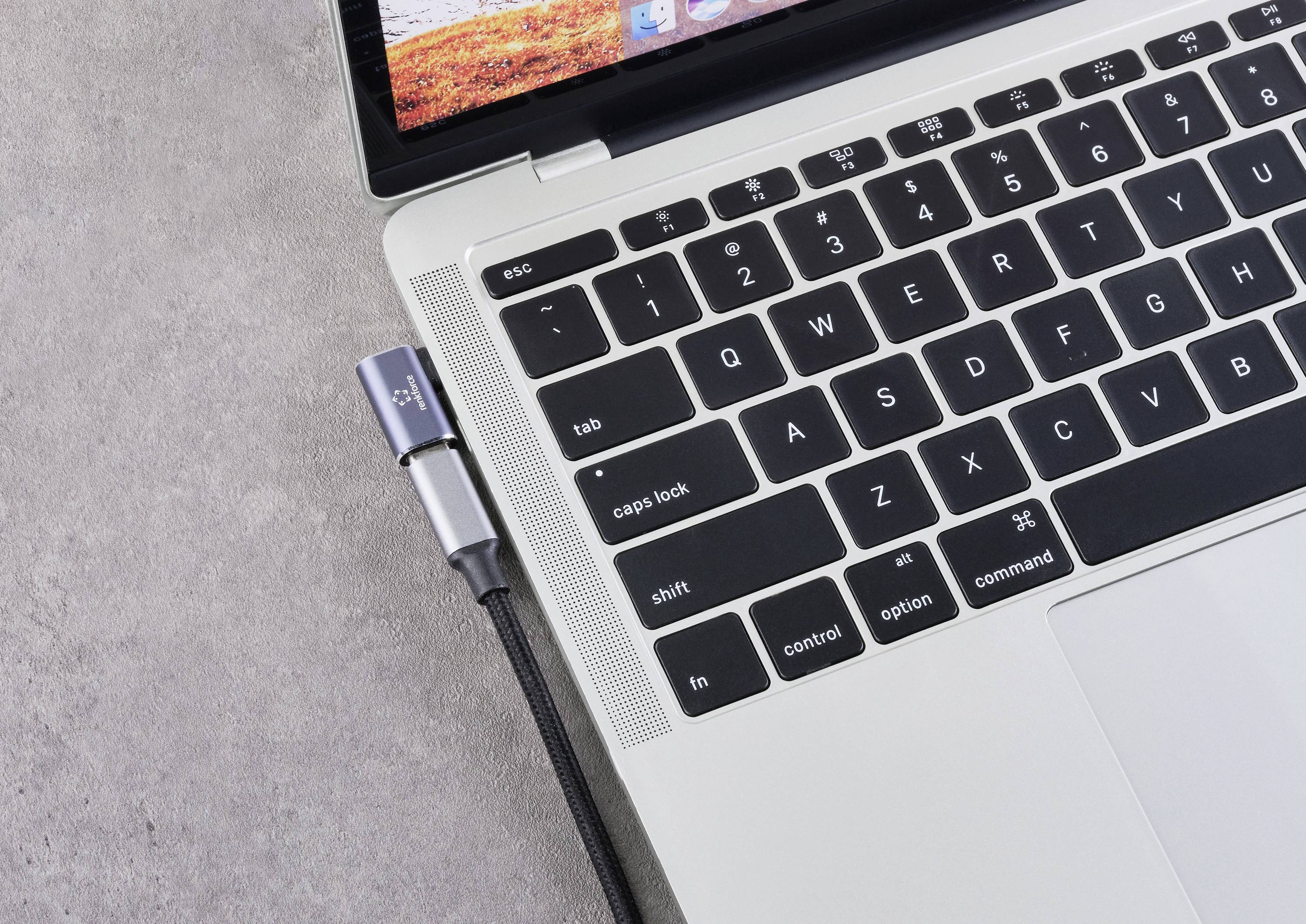 A laptop keyboard with a USB cable connected on the left side, on a grey surface.
