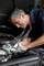 A mechanic is repairing a car's engine. He is wearing a head torch around his neck that illuminates the work area.
