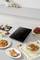 A table with an induction hob in the centre, surrounded by various plates of fish, vegetables and meat dishes.