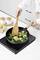 A person is frying prawns and broccoli in a pan on an induction hob. Nearby are seasoning shakers and corn on the cob.