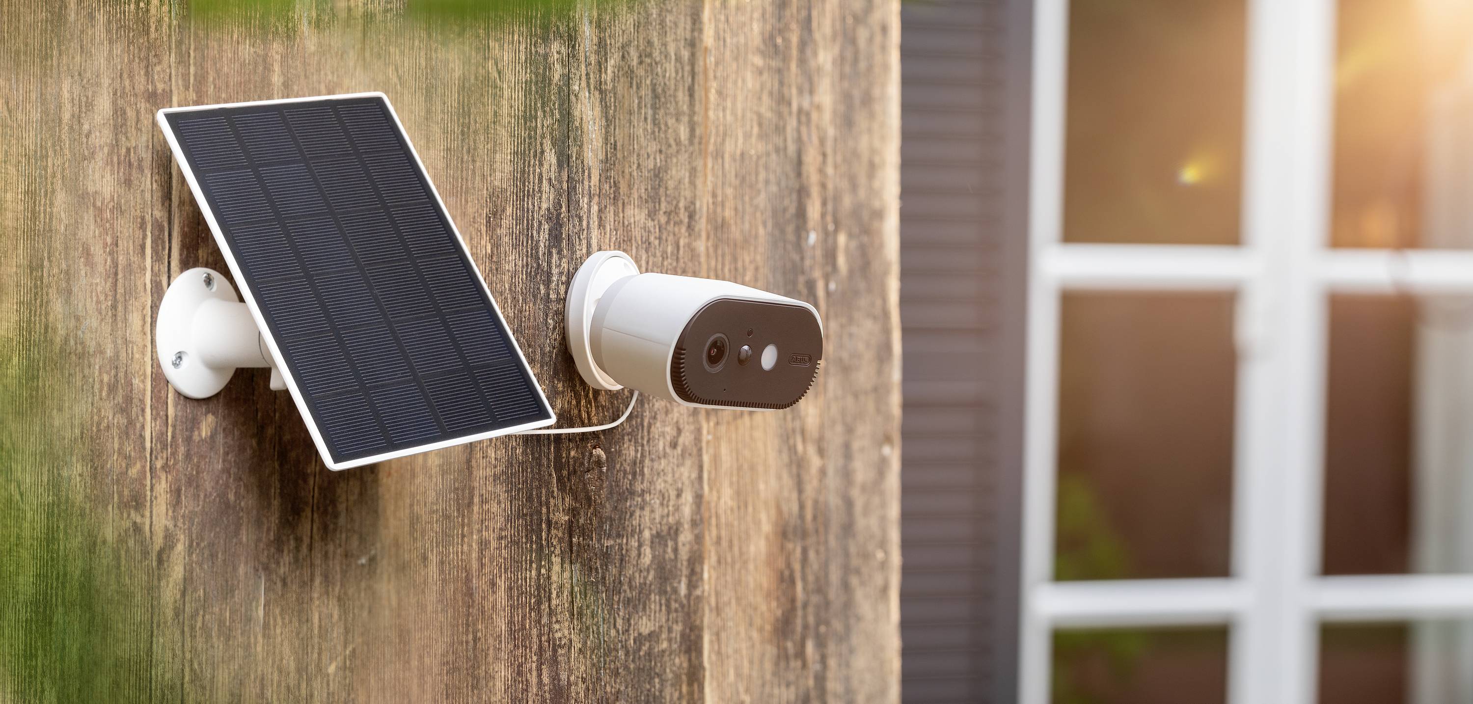 Outside camera and solar panel mounted on a house facade, with a window in the background.