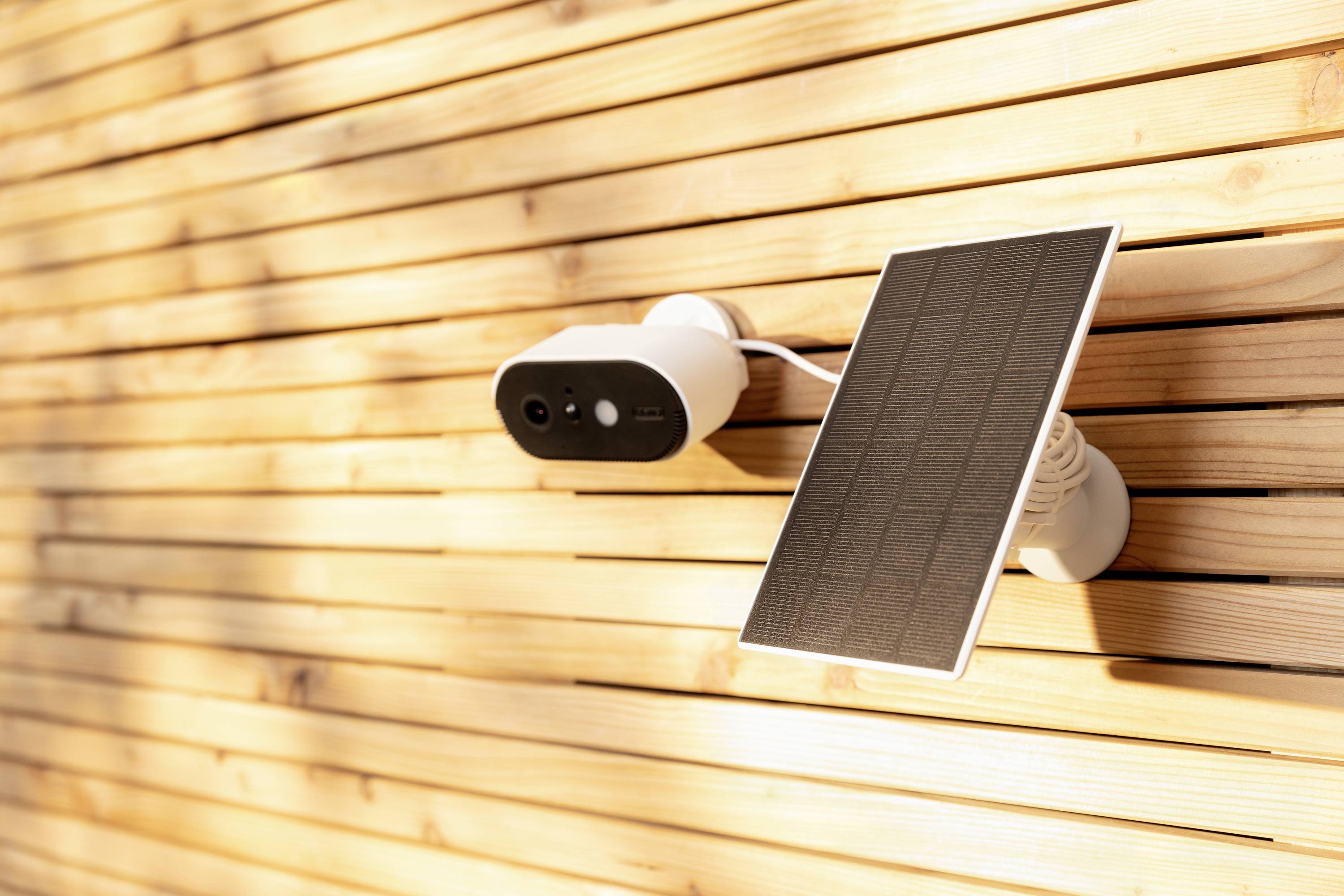 Solar-powered security camera mounted on a wooden facade, surrounded by warm sunlight, symbolising sustainable surveillance.