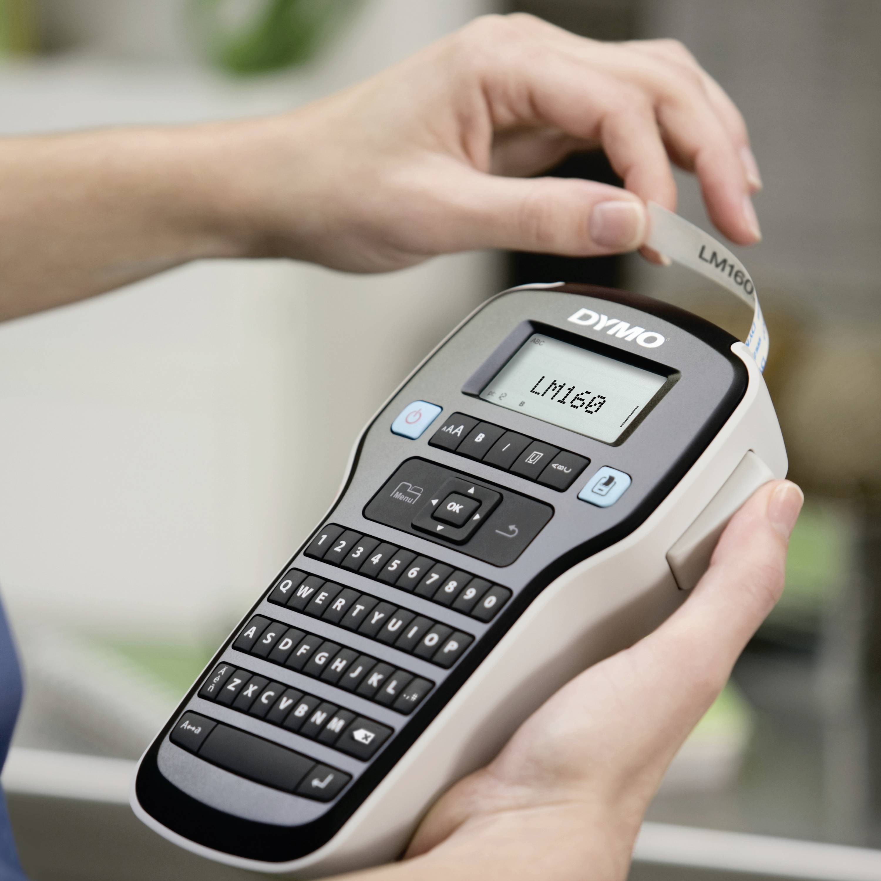 A person is holding and using a label printer that is printing a new label. The display shows text while the label is emerging.