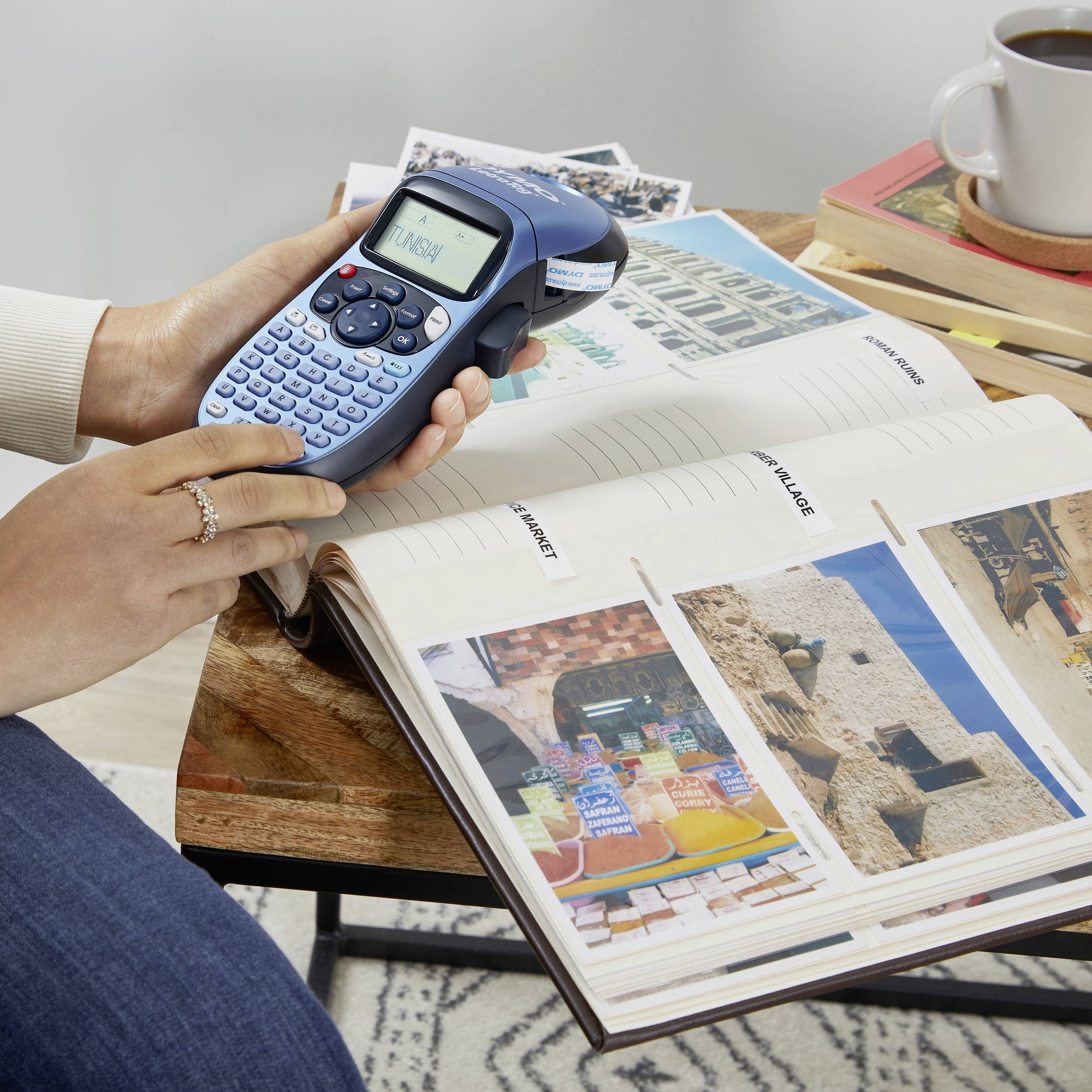 A person is using a label maker to label folders. On the table, there are folders, a book, and a mug.
