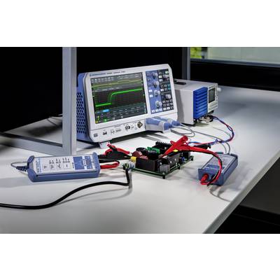 'An oscilloscope shows a graphical representation of voltage signals, connected with electronic components on a table.'