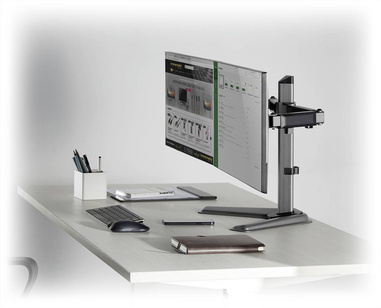 A stylishly arranged desk with a computer monitor, keyboard, notebook, and pen holder on a modern white table.