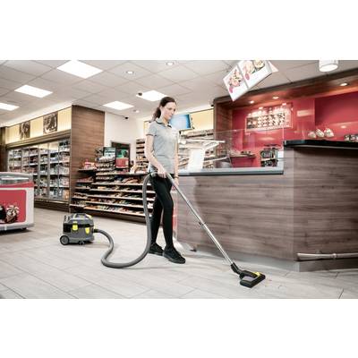 A person vacuuming the floor in a convenience store, with shelves of products and a counter in the background, indicating a cleaning routine.