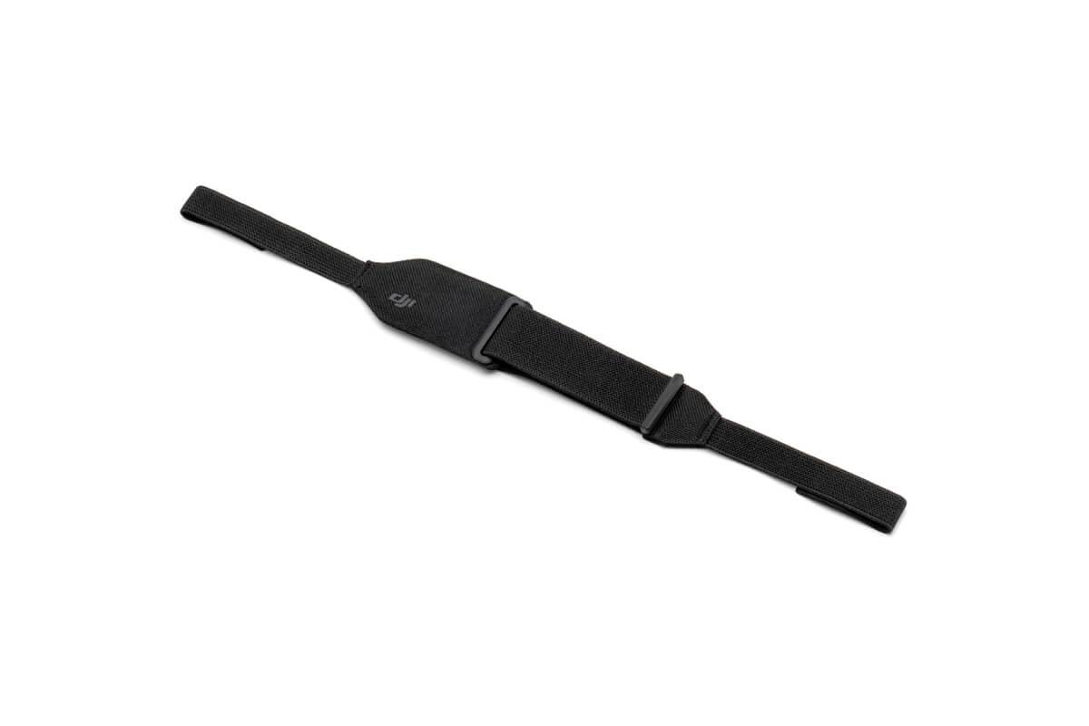 A black, adjustable wristband lies on a white surface. It is composed of multiple segments with hook and loop fastening.