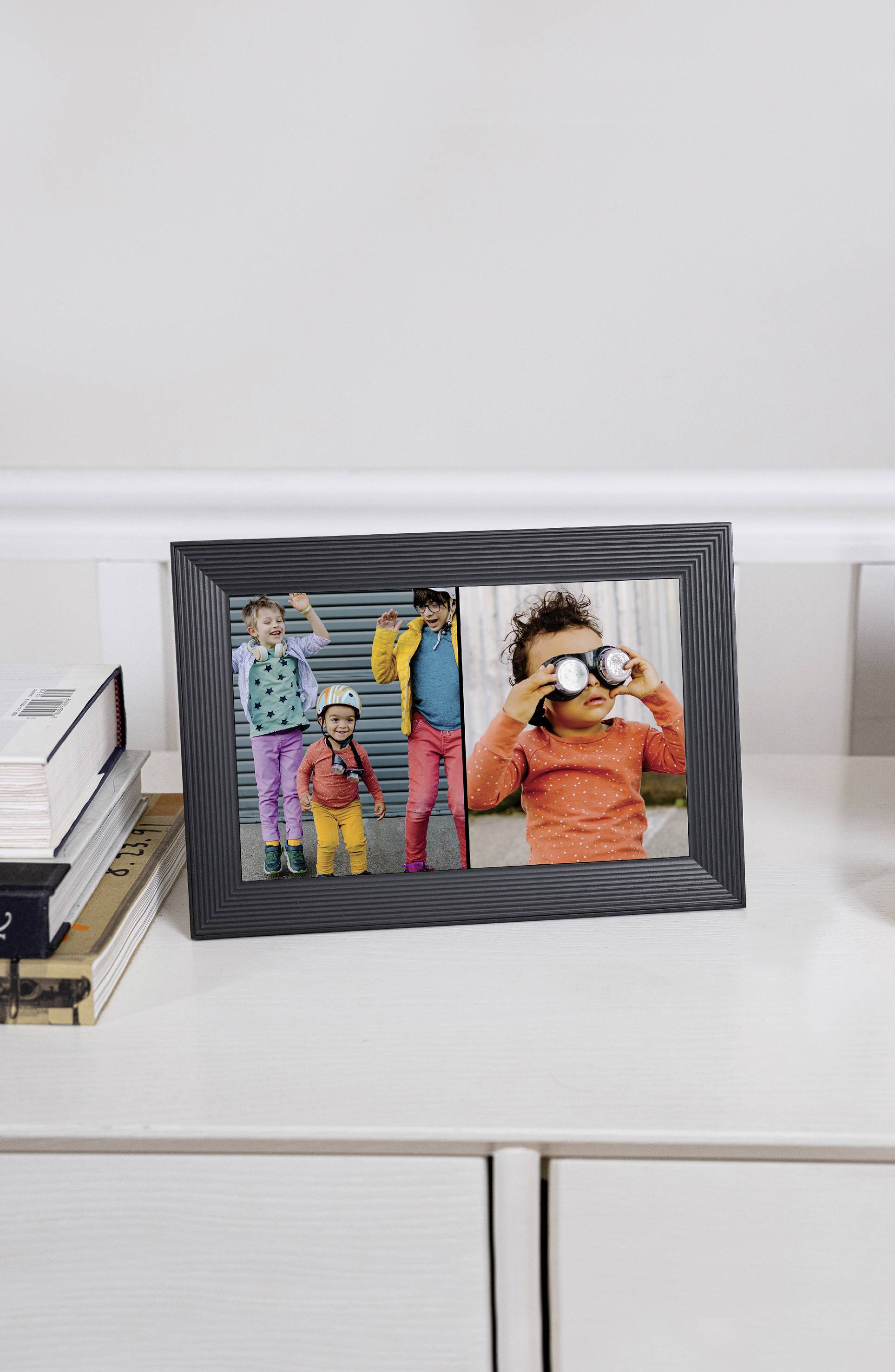 A photo frame with two pictures: On the left, four children in colourful clothing, on the right a child looking through binoculars. The frame is sitting on a sideboard.