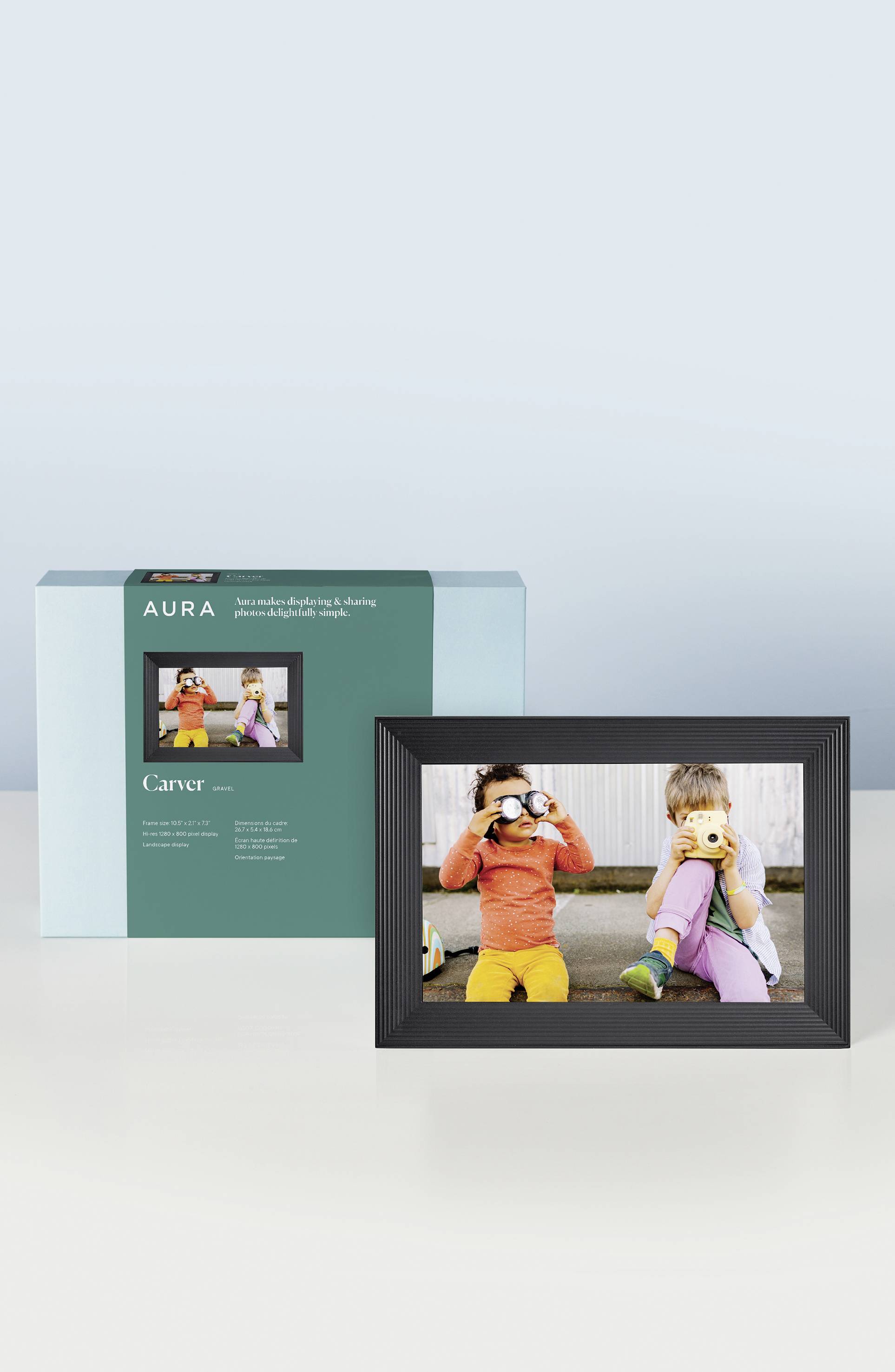 Two children are sitting outside on a pavement, one with binoculars, the other with a cuddly toy. The frame is positioned in front of the packaging.