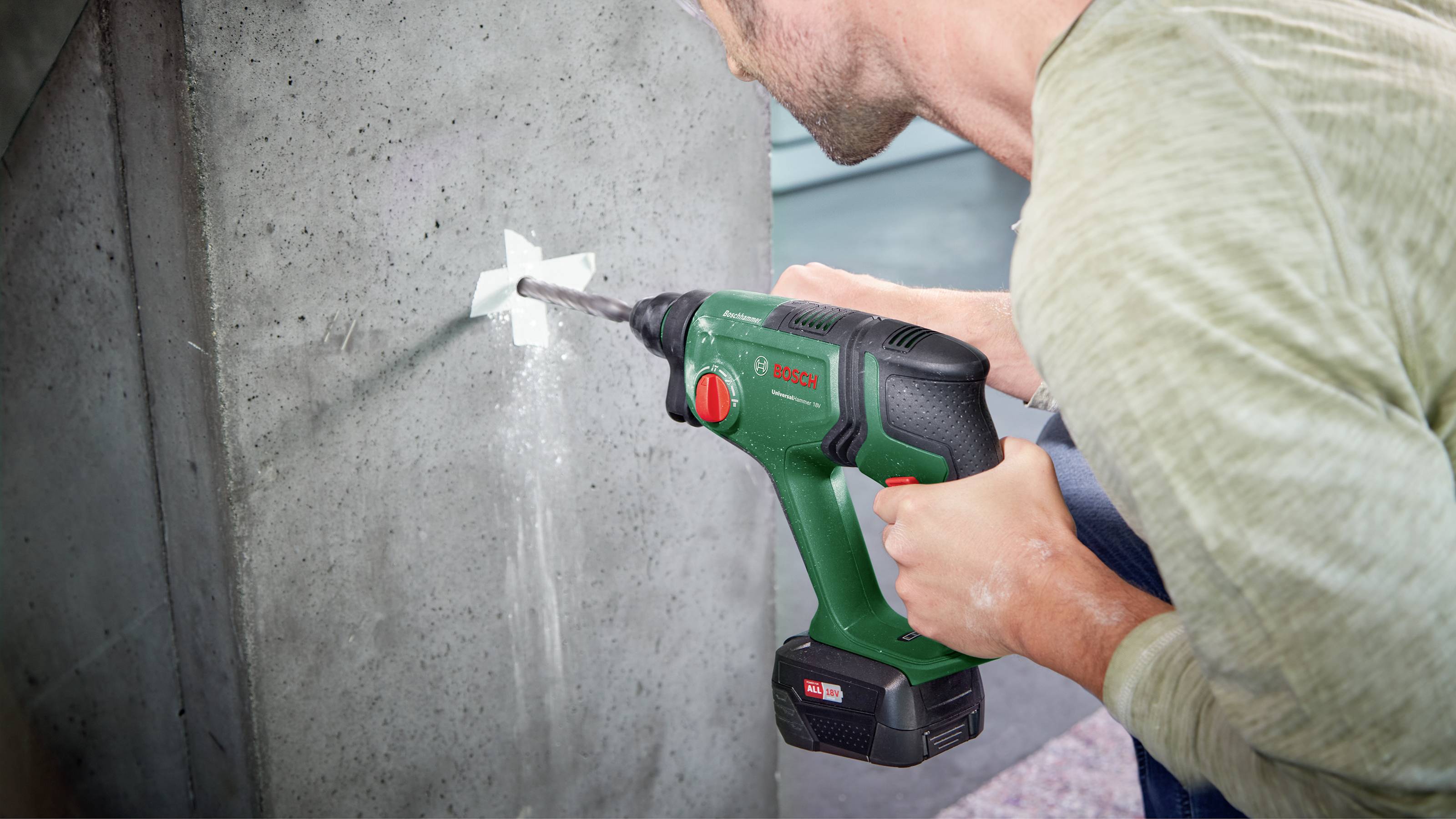 A man is drilling a hole in a concrete wall using a green drill. The scene depicts the drill in action during a DIY project.
