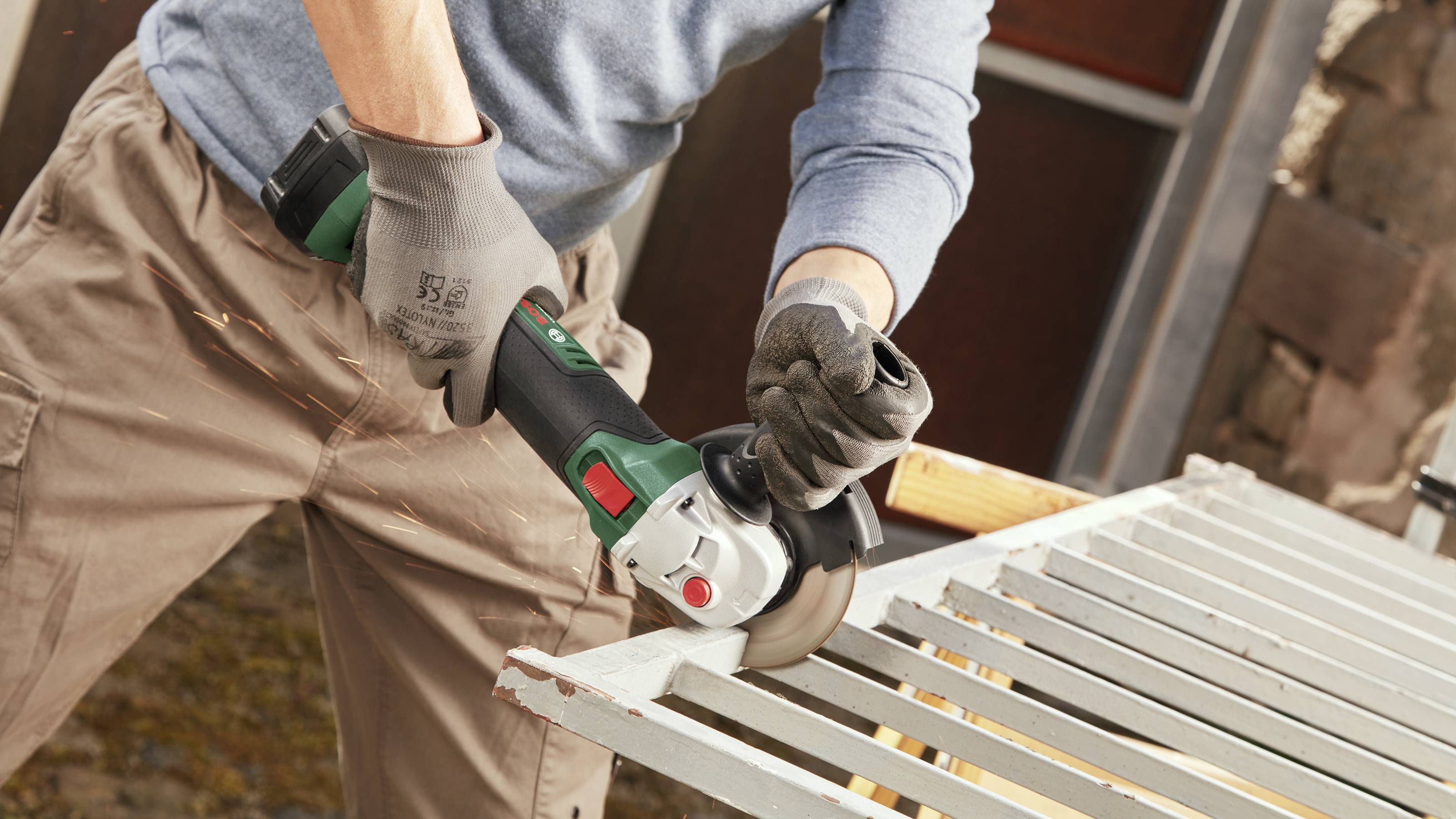 A person is cutting metal rods with an angle grinder. Sparks are flying from the cutting point. They are wearing safety gloves.