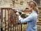 A woman is grinding an old iron gate with an electric grinder. She is wearing safety glasses and ear protection in a rustic setting.