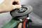 A hand is securing an abrasive disc to an angle grinder. The background is out of focus, with the tool in sharp focus.
