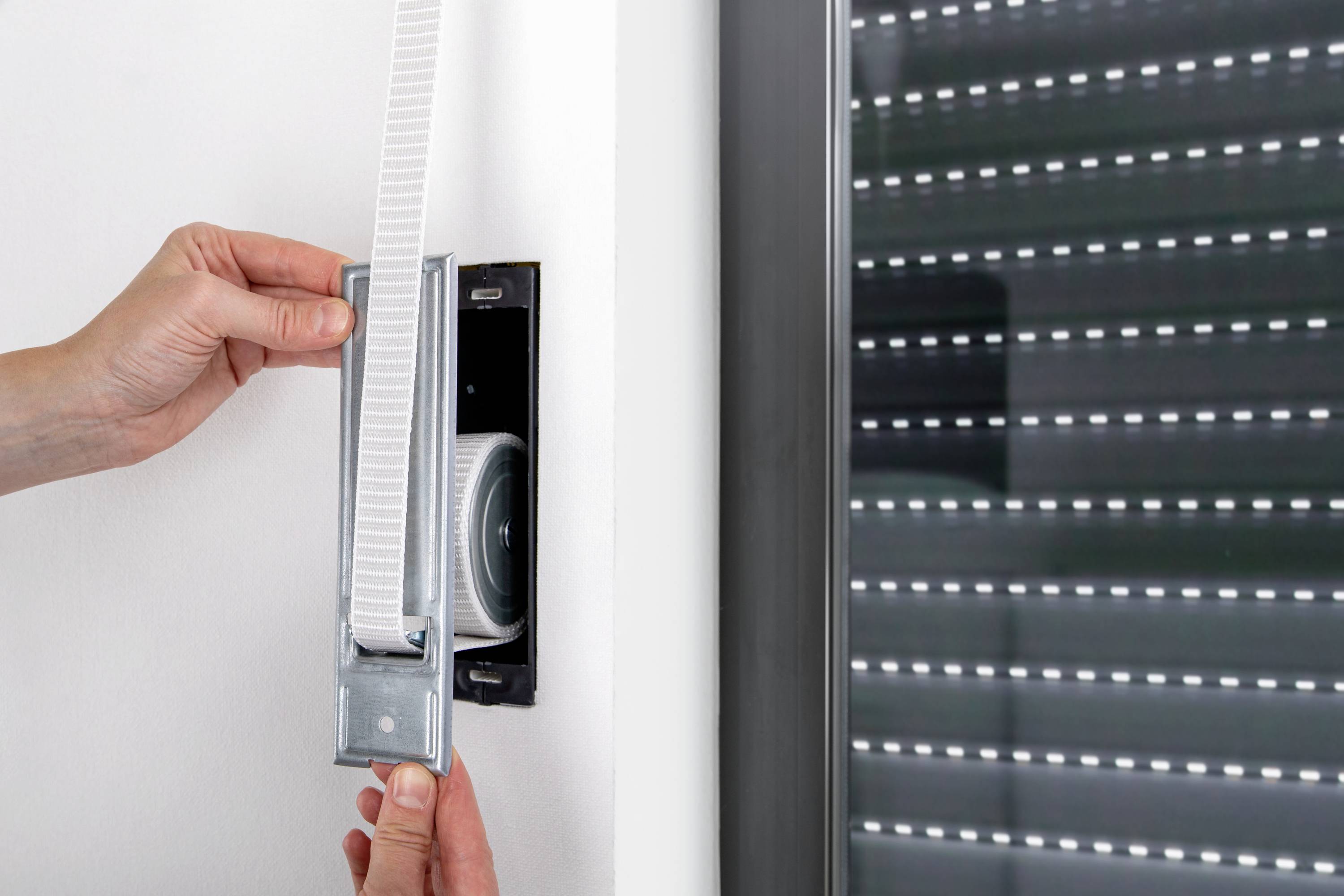 A person installs or repairs a blind on a window by inserting the webbing into a wall bracket.