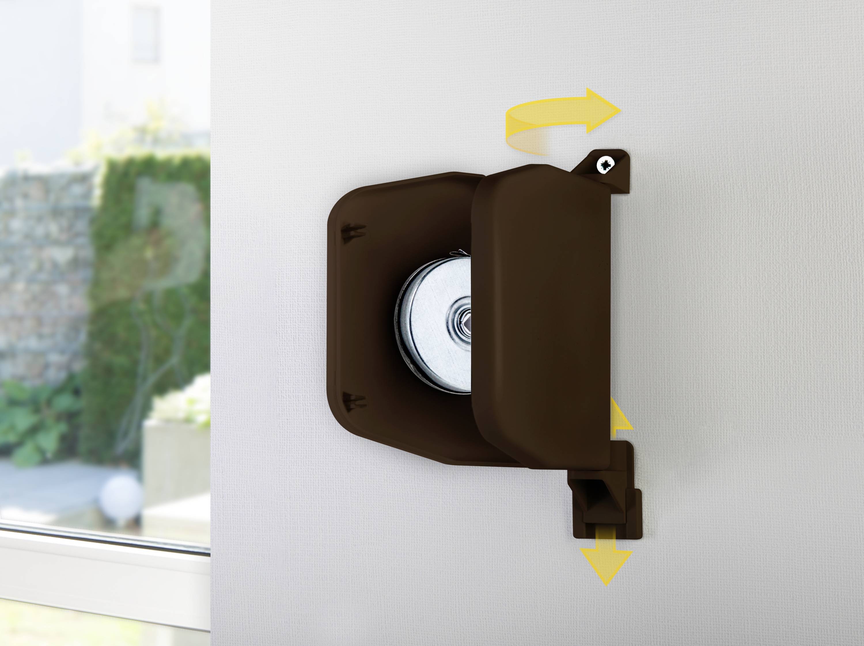 Brown belt winder mounted on a white wall, with yellow arrows indicating the belt winding direction for a roller shutter system.