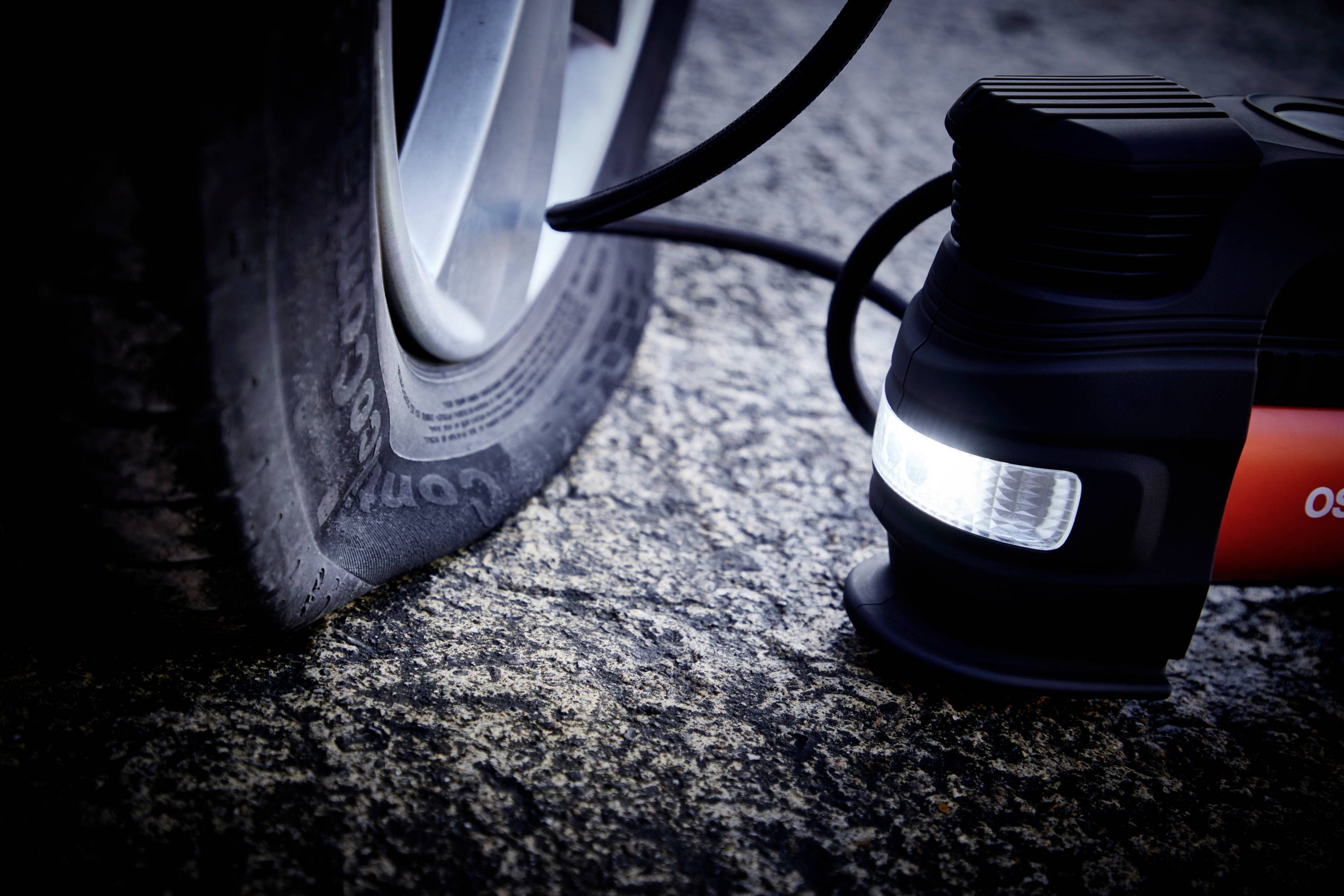 Close-up of a car tyre that is partially flat, with an attached tyre compressor inflating the tyre.