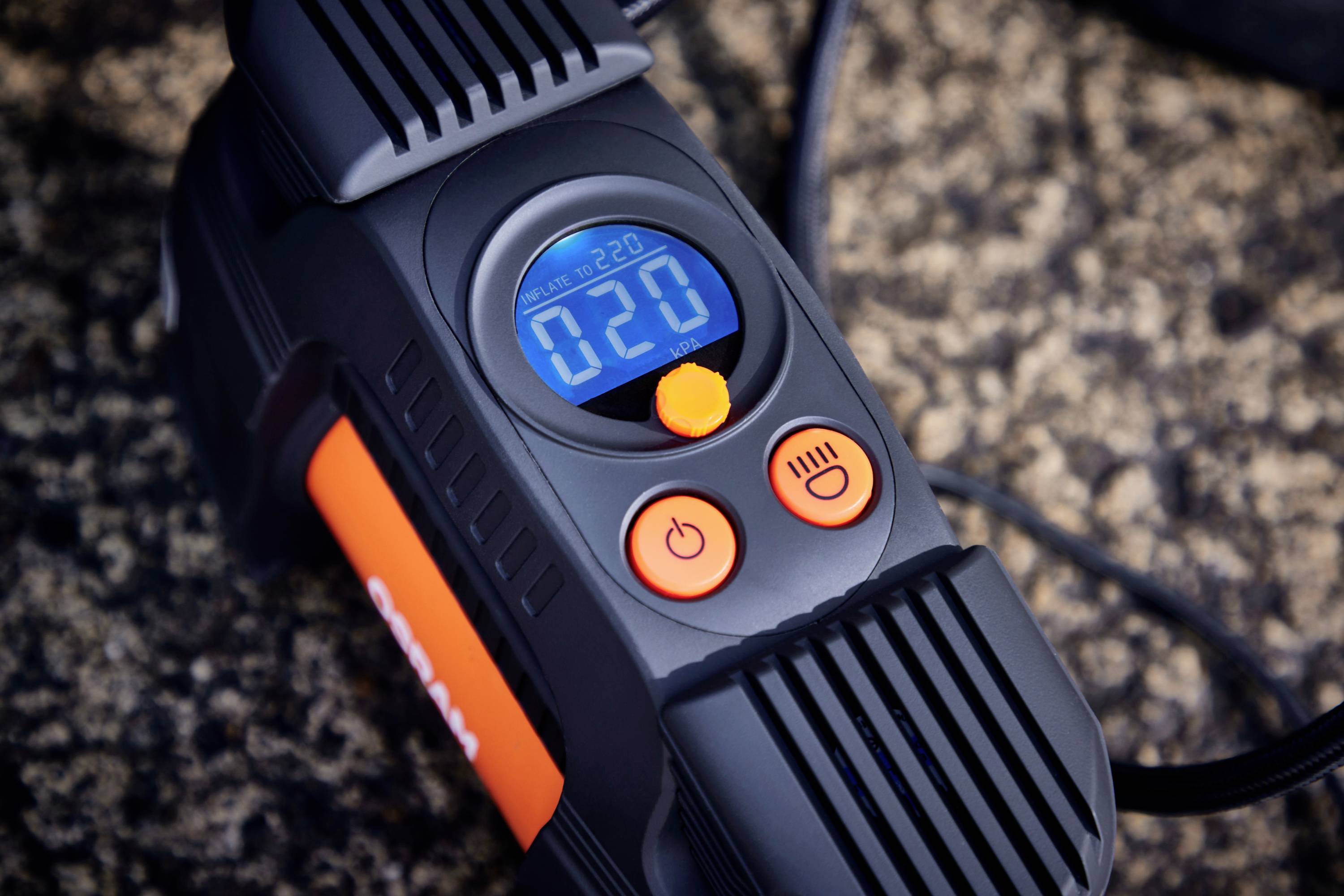 A portable air compressor with a digital display shows '020'. It has orange control buttons and black ventilation slots.