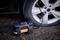 A portable air compressor is inflating a car tyre. The black compressor displays a digital readout and is switched on.