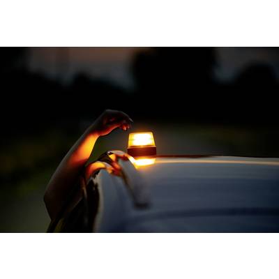 A hand reaches out of a car and adjusts an orange warning light on the roof. The surroundings are dark.