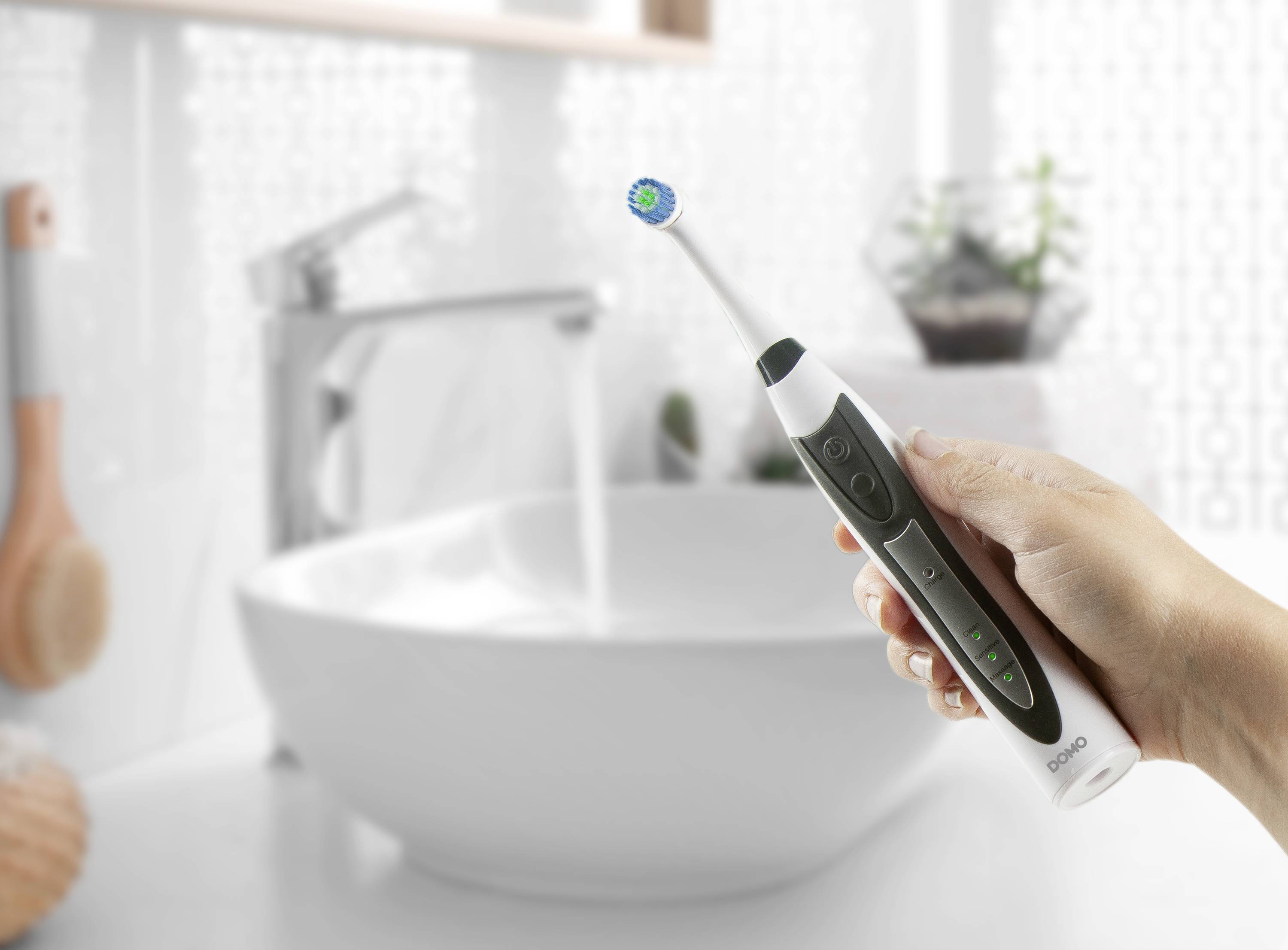 A person is holding an electric toothbrush by a sink in the bathroom.