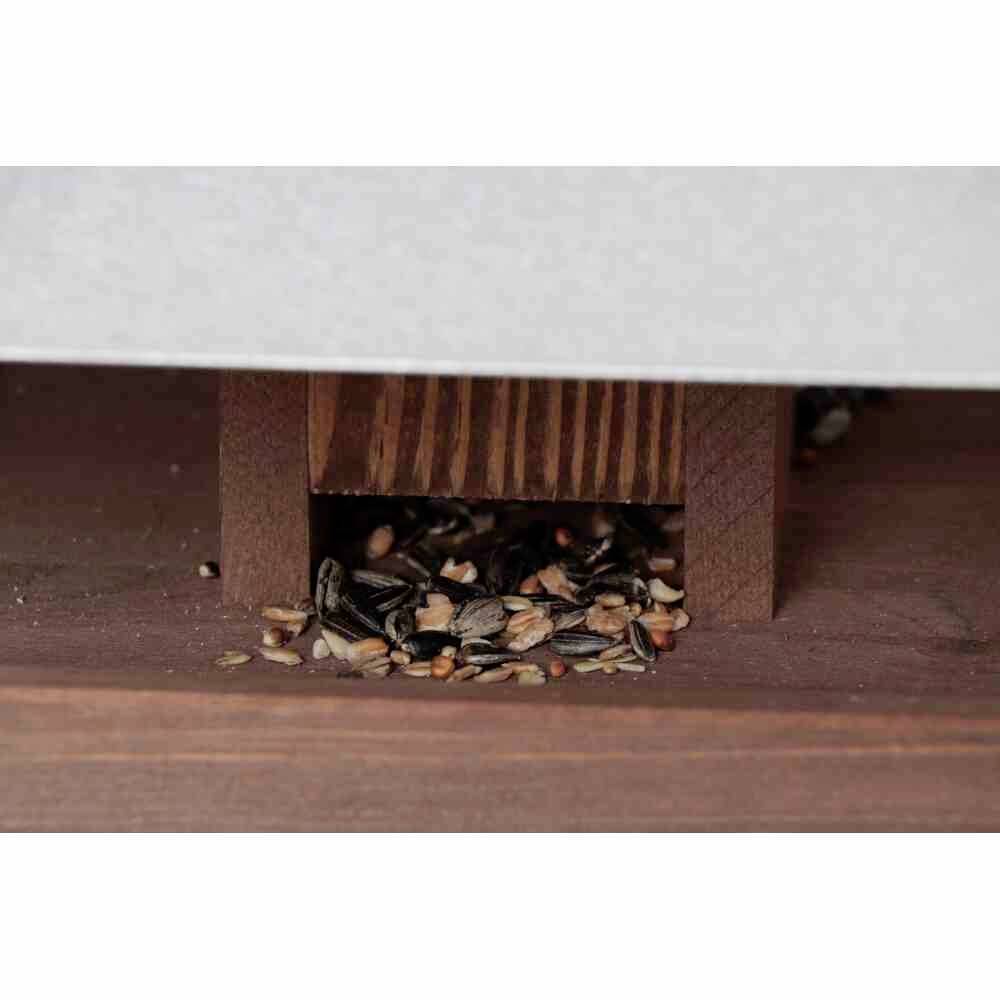 Bird feed lies ready under a wooden roof, with a mixture of sunflower seeds and other seeds.