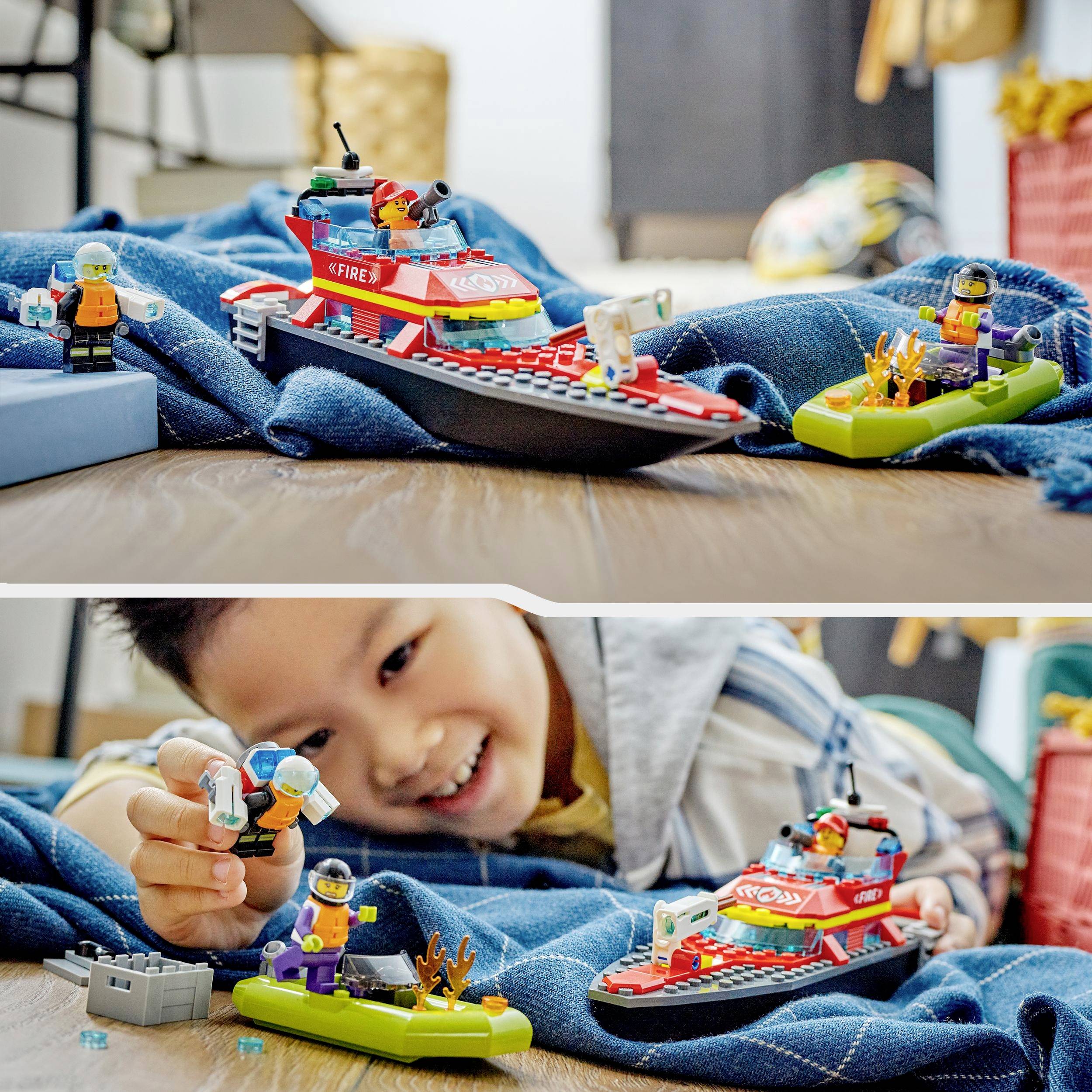 A child happily plays with toy boats and figures on a table. One of the boats has a 'FIRE' label.