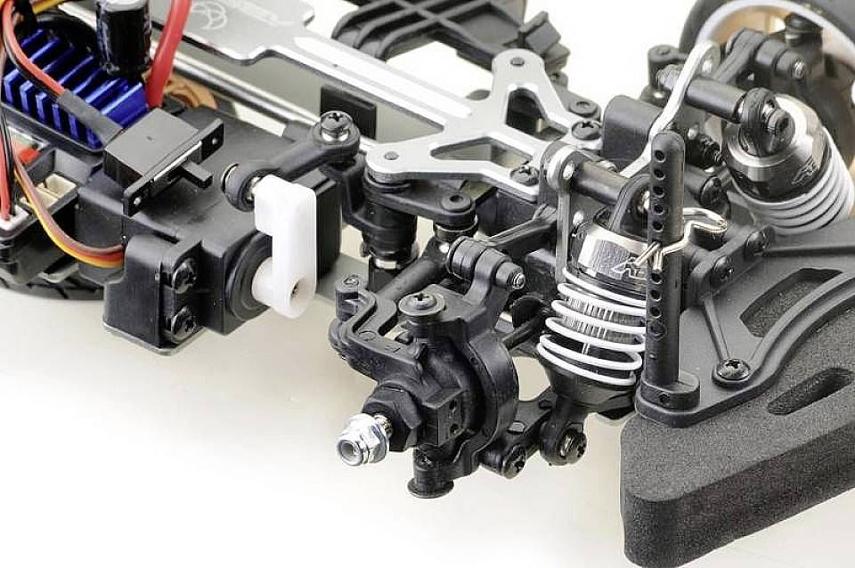Close-up of a complex model car chassis with visible shock absorbers, springs, and electronic components.