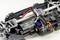 Close-up of a remote-controlled model car chassis. An electric motor, wiring, and control electronics are visible on a metal frame.