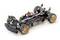 An open chassis of a remote-controlled car displays wheels, suspension, and electronic components on a white surface.