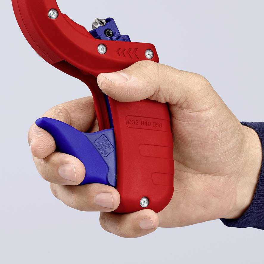 A hand is holding a red pipe cutter with a blue handle, ready to cut pipes. The cutter has an integrated ratchet function.