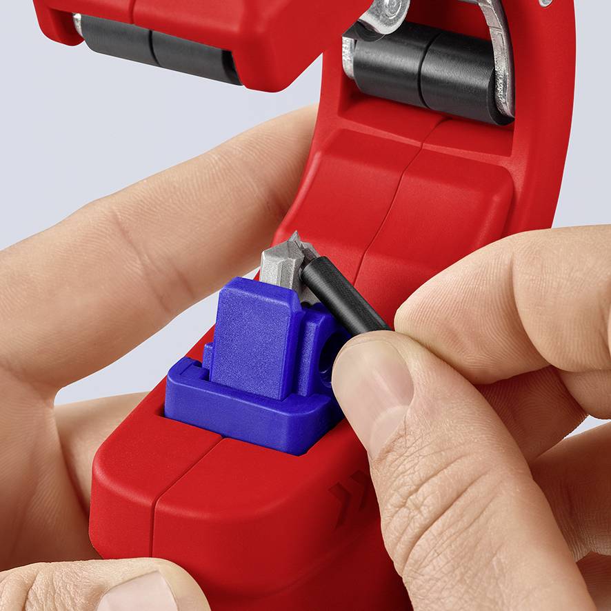 'Hands are operating a red cable stripping tool with a blue component and a blade to precisely strip a cable.'