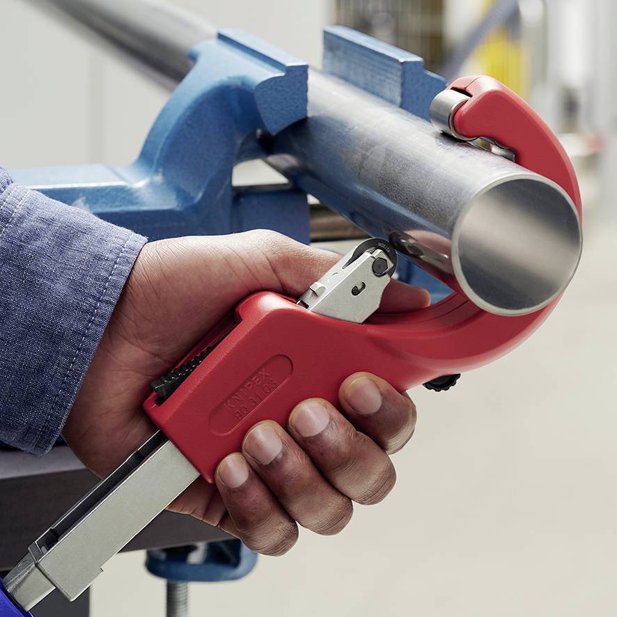 A person is cutting a metal pipe with a pipe cutter. The pipe is held by a blue clamping system.