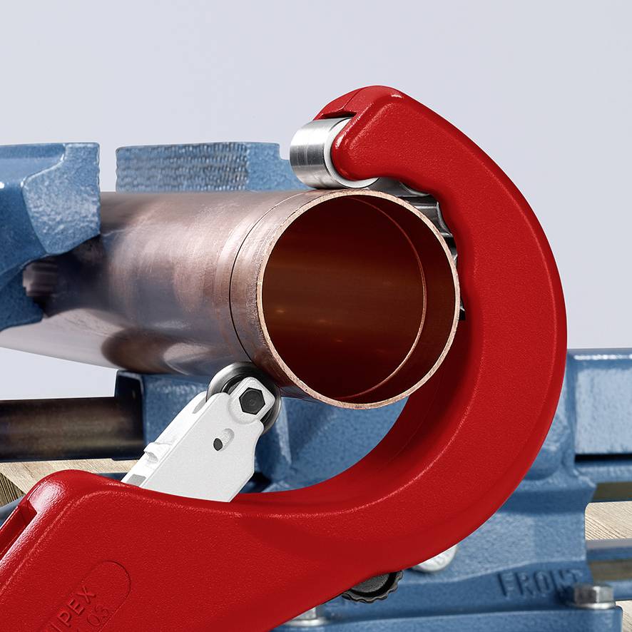A copper pipe is being cut by a pipe cutter with a red handle. The pipe is resting on a blue vice.