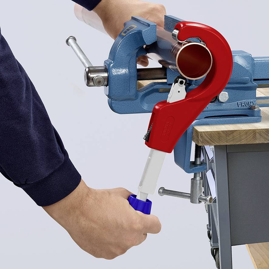 A person is cutting a plastic pipe with a red pipe cutter, which is secured in a blue vice.