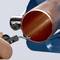 A hand using a pipe deburring tool on a copper pipe. The tool removes sharp edges to create a smooth surface.