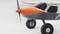Close-up of a model aeroplane with an orange-grey nose and a propeller. The aeroplane has large wheels and is standing against a white background.