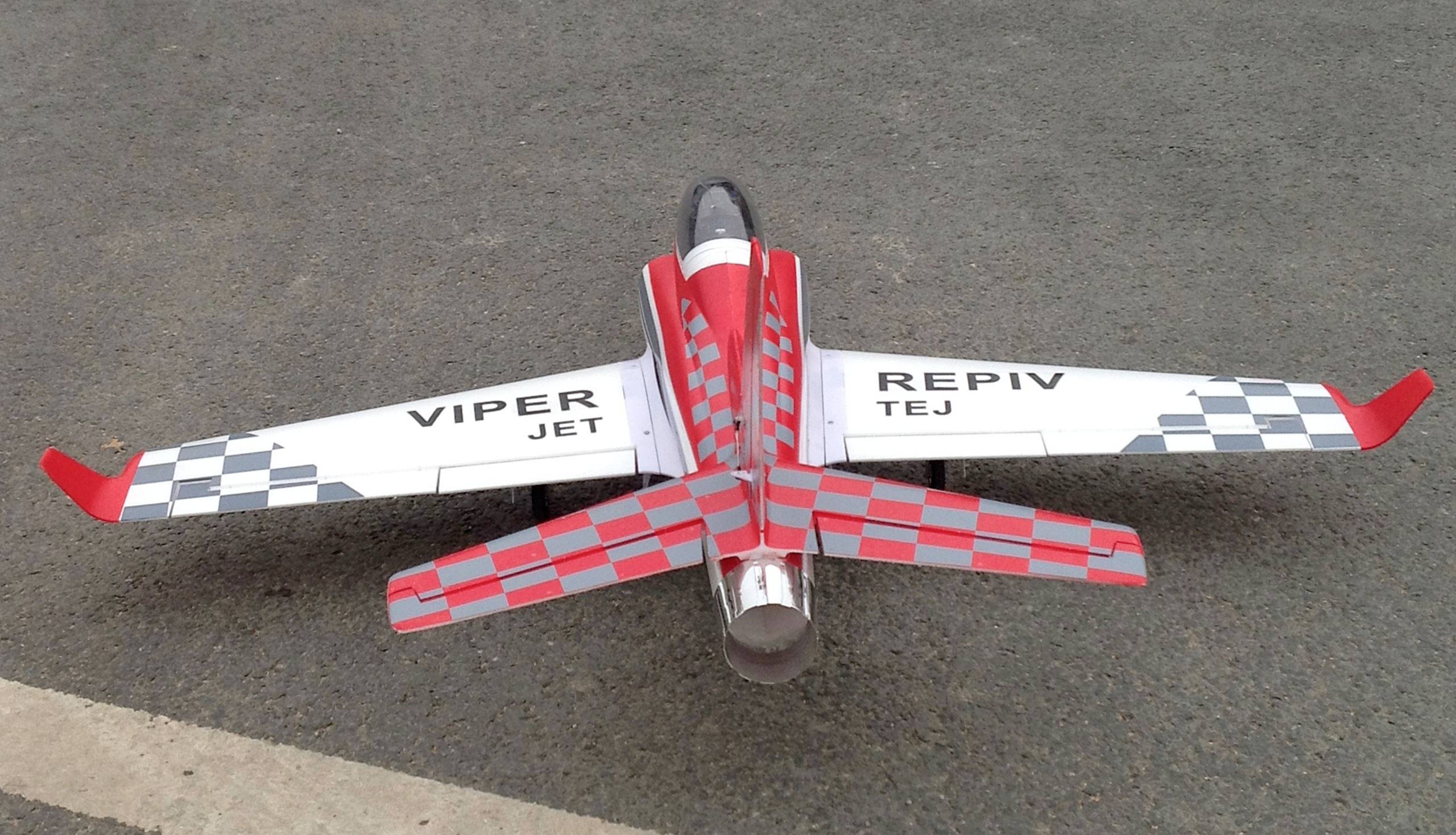 A small model aeroplane with a red and white chequered pattern and the inscription 'VIPER JET' on the wings is standing on the road.