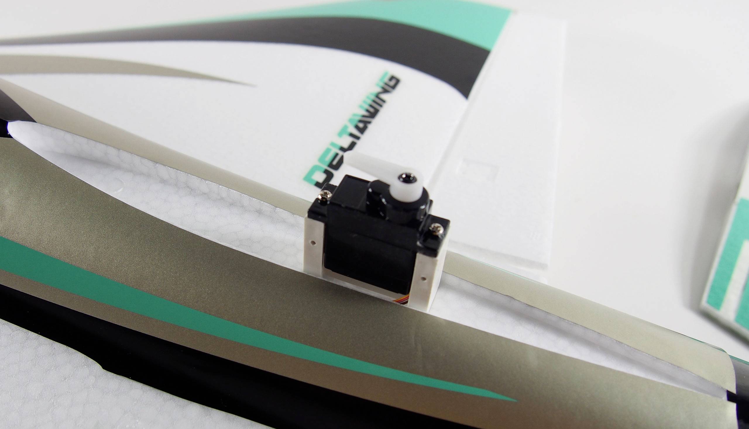 A remote-controlled aircraft part with an integrated servo and the inscription 'DELTAXWING' in green lettering.