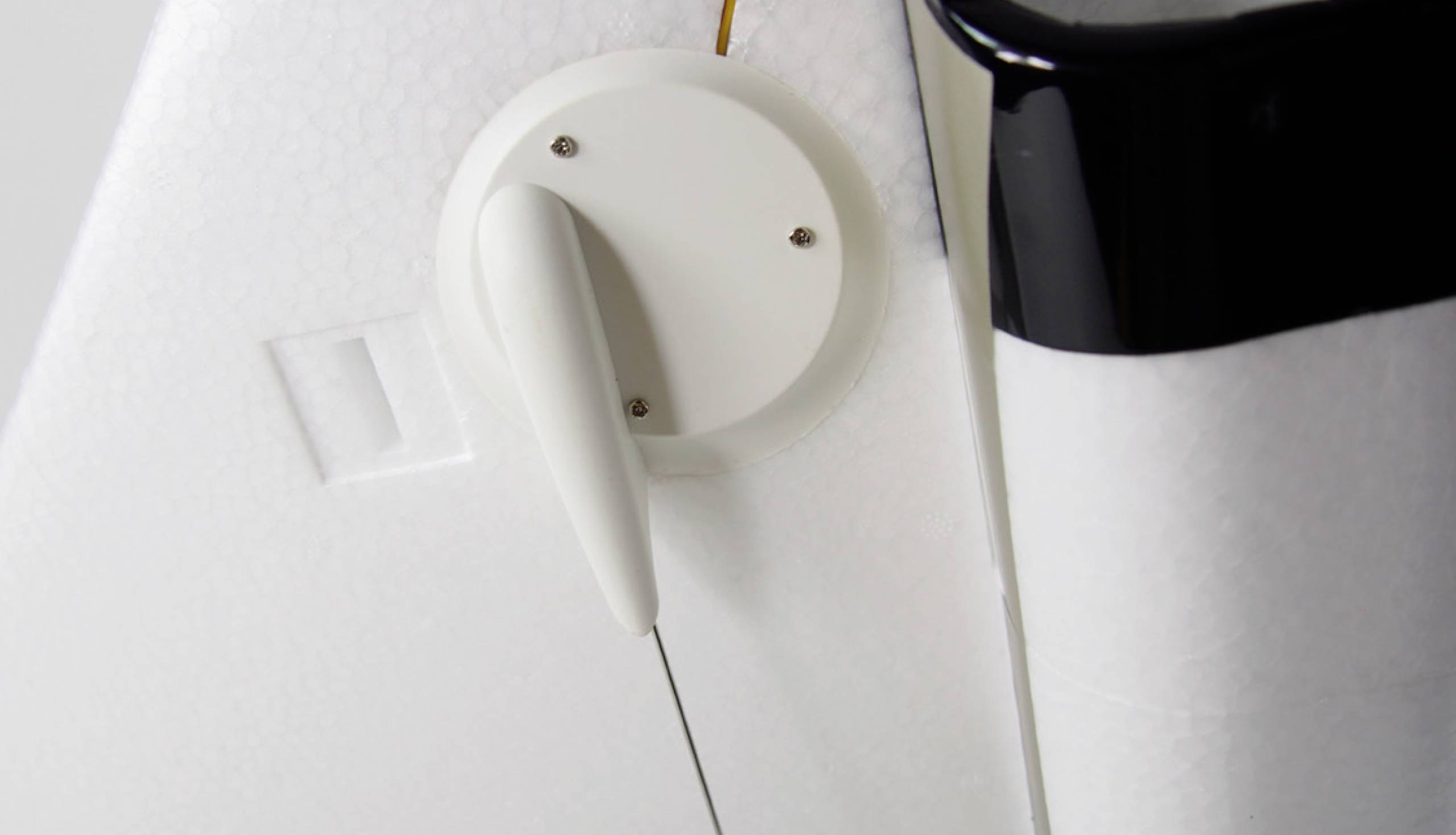 Close-up of a white component of a model with a black stripe and a round button on the side, potentially an aircraft part.