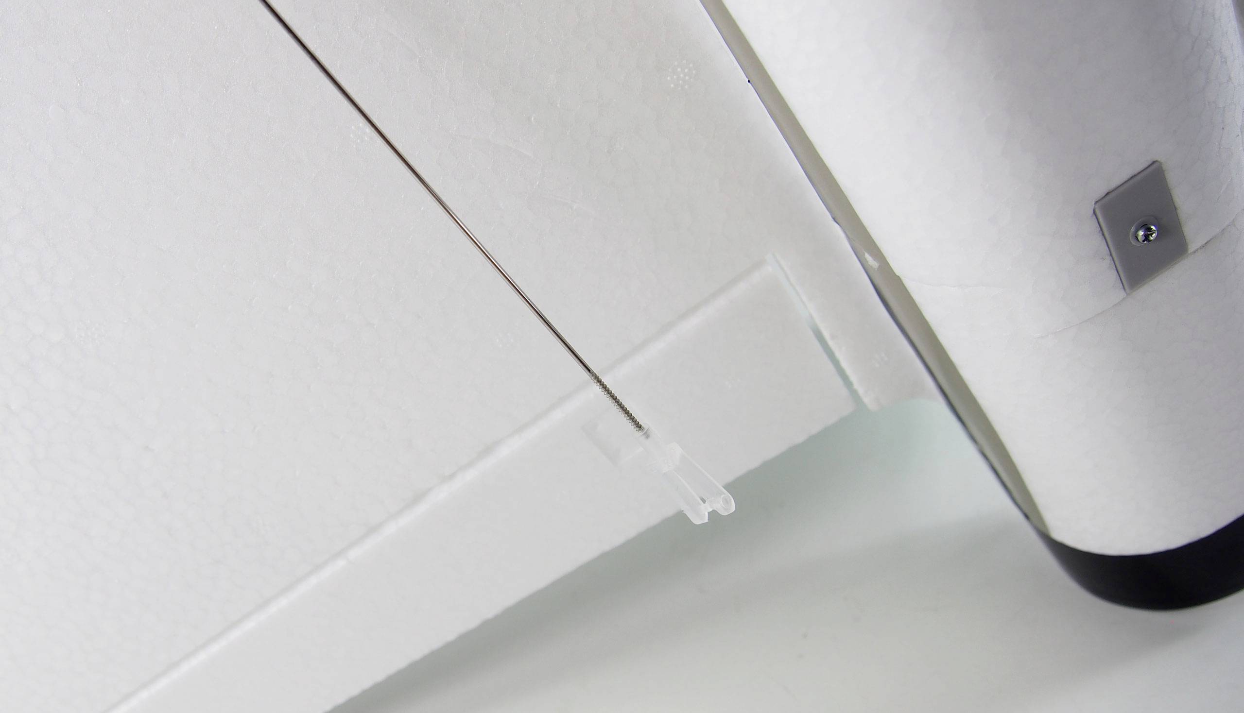 A white surface with a thin, diagonally positioned metal rod. A metal edge is located on the right side of the image.