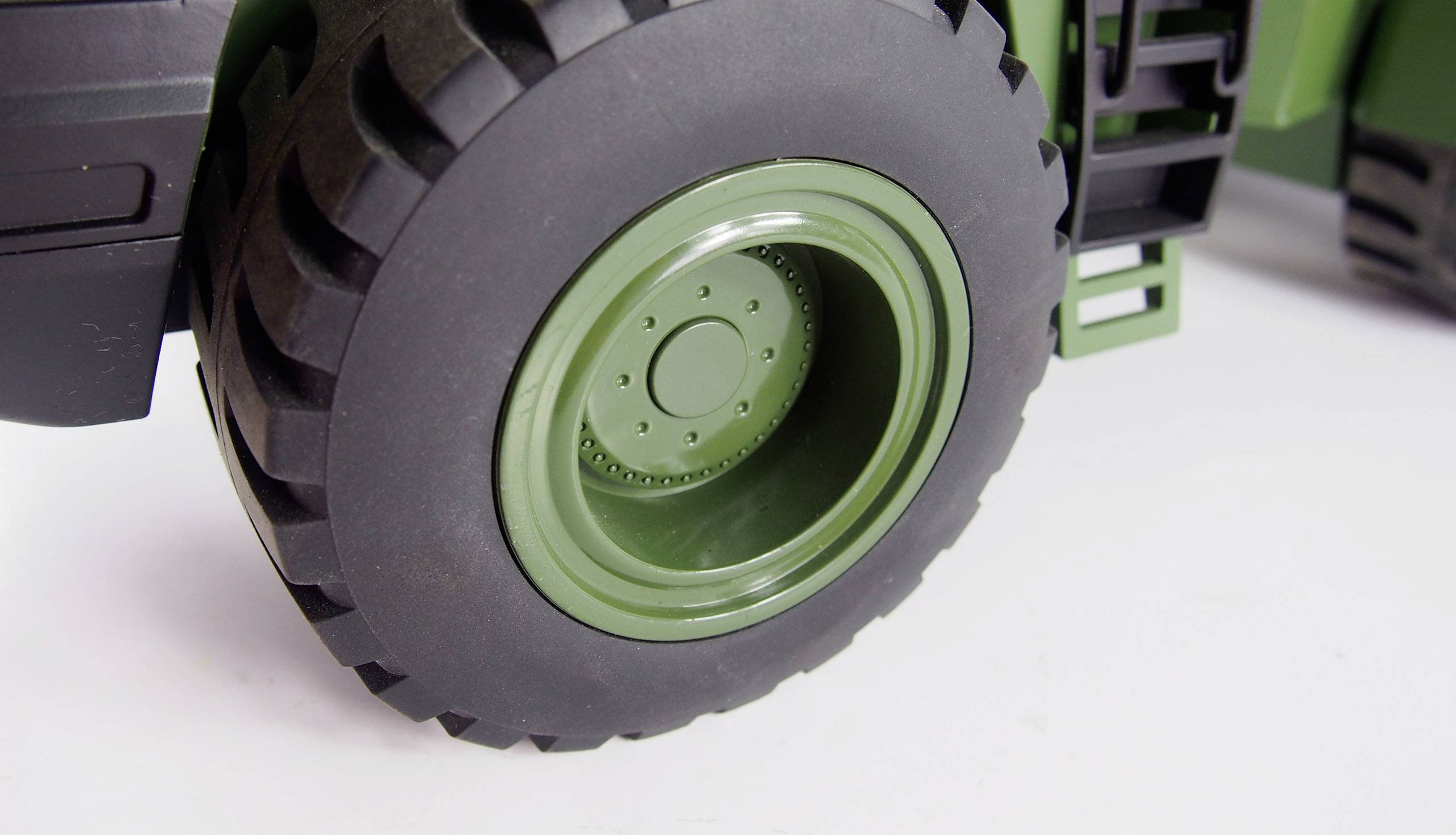 Close-up of a robust, black tractor tyre with a green wheel rim on a white background.