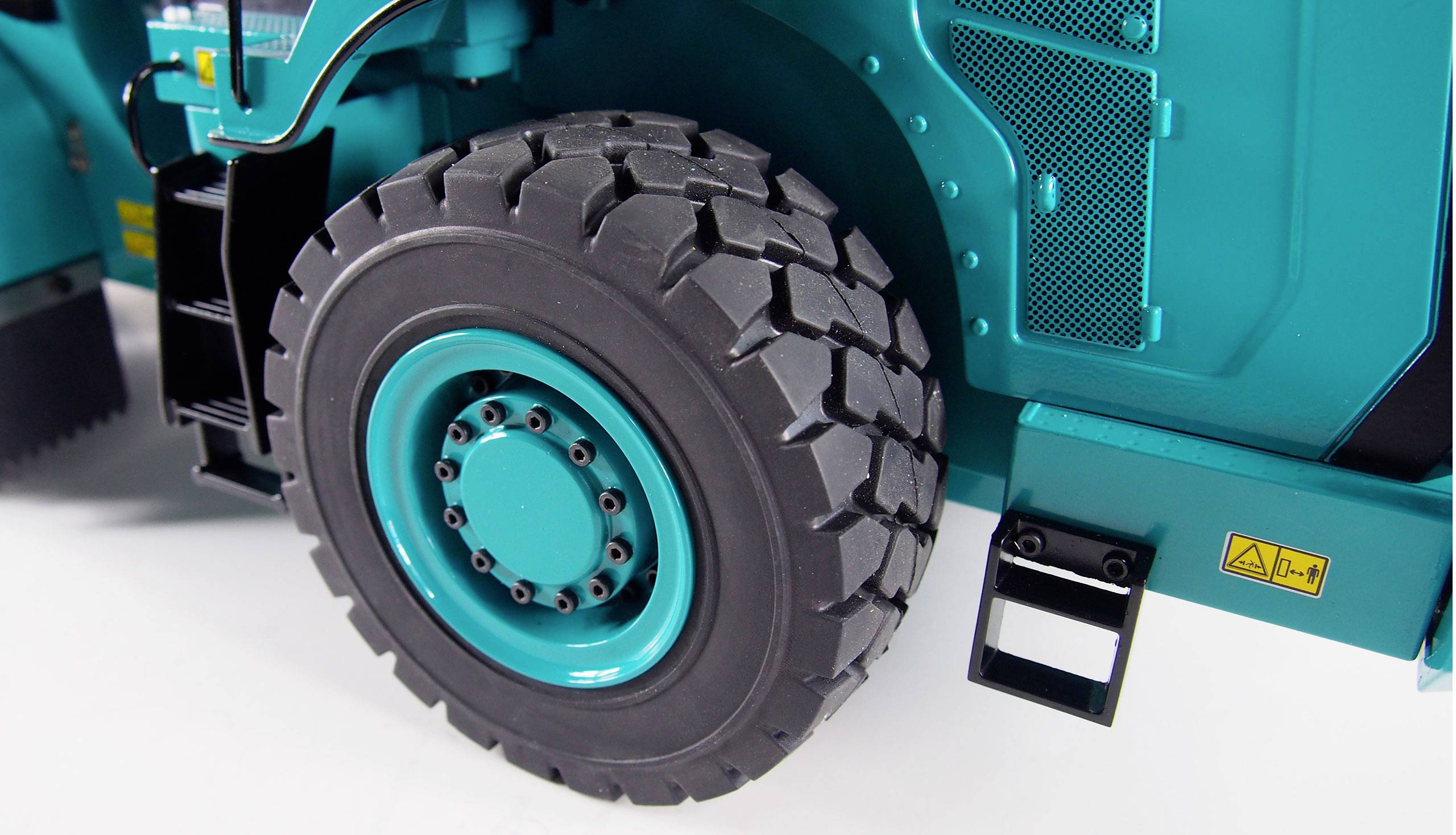 Close-up of a dark grey tyre on a turquoise vehicle, possibly an industrial machine. Some details are visible.