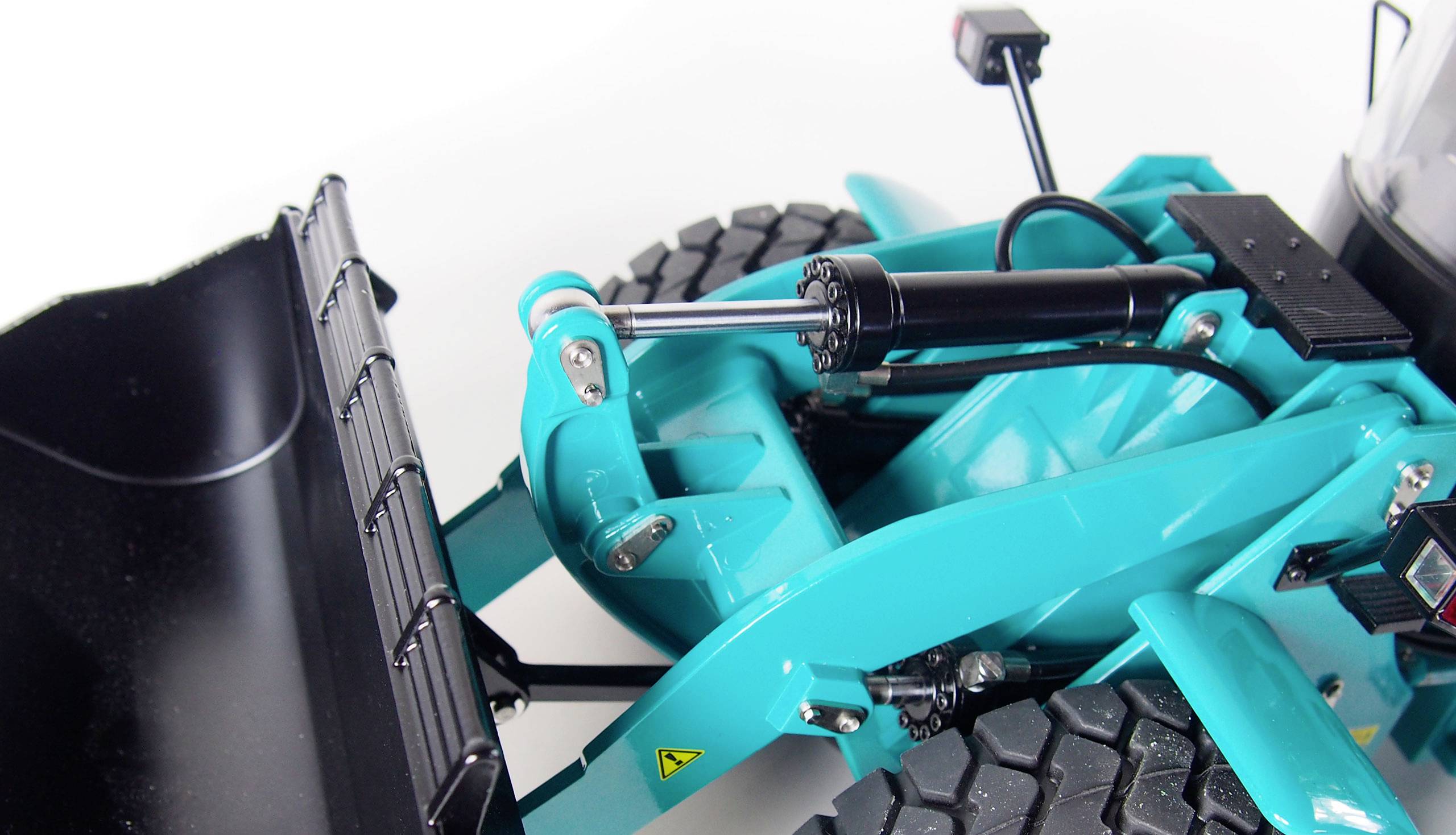 Close-up of a light blue bulldozer facing a white background. The bucket, hydraulic system, and tyres are visible.