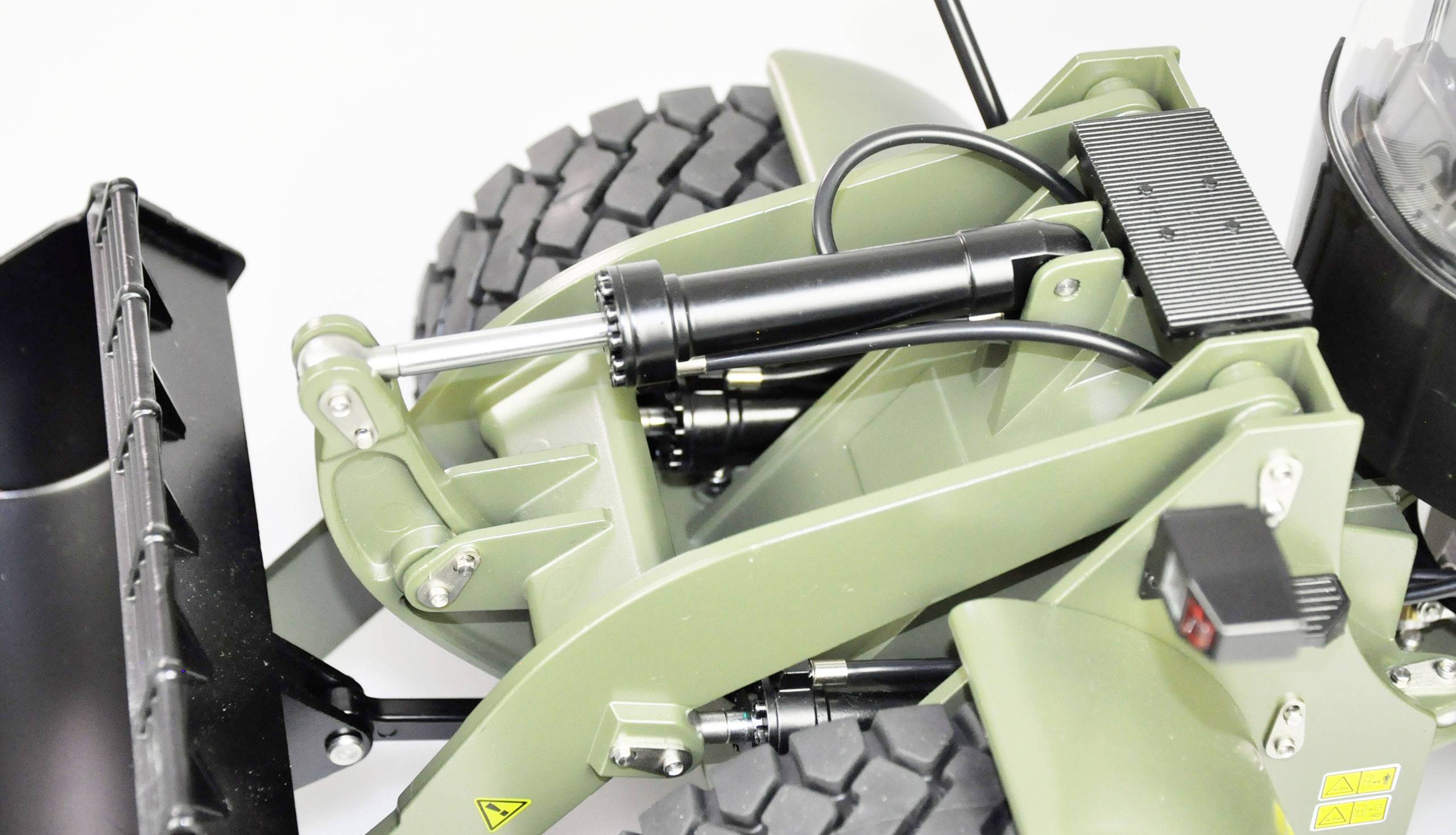 Close-up of a green model wheeled loader front, showing the hydraulic cylinder and dozer blade in front of a robust tyre.