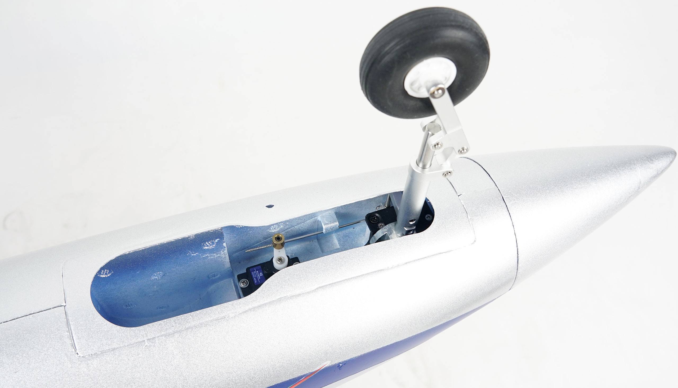 Close-up of a model aircraft fuselage made of metal, with a detailed view of an extended undercarriage and an open cover.