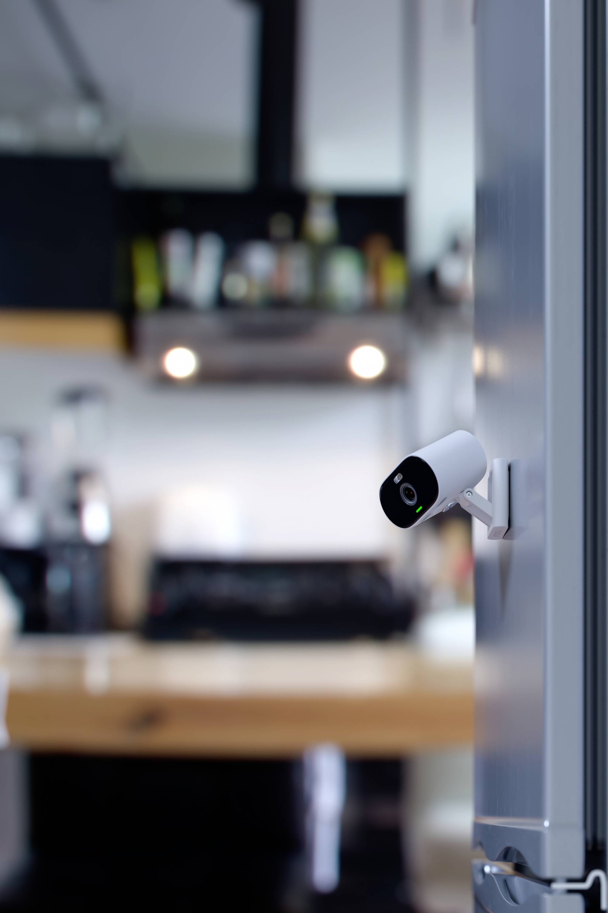 Security camera mounted on a fridge, showing the interior of a modern kitchen with blurred appliances in the background.