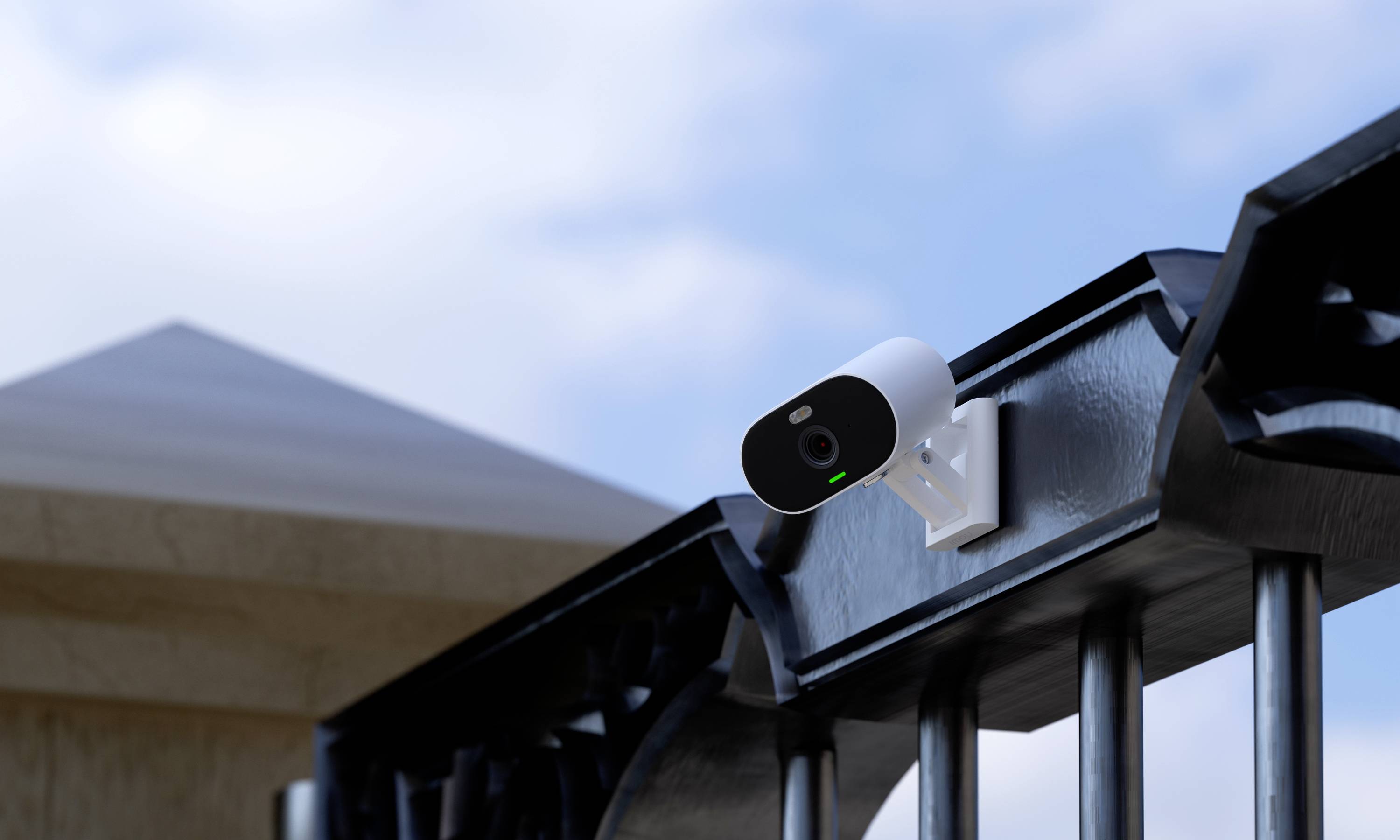 Security camera mounted on a metal fence, monitoring the entrance area of a building under a blue sky.